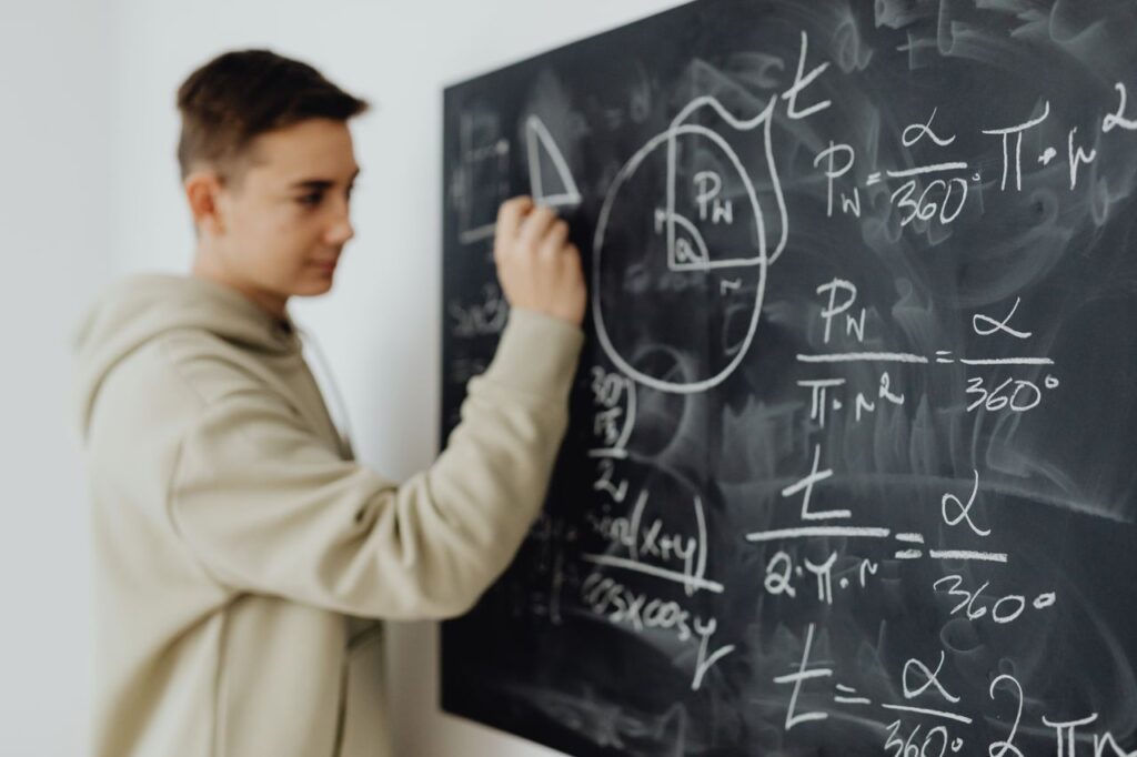 Focused teenager solving a math equation on a blackboard in a classroom setting.